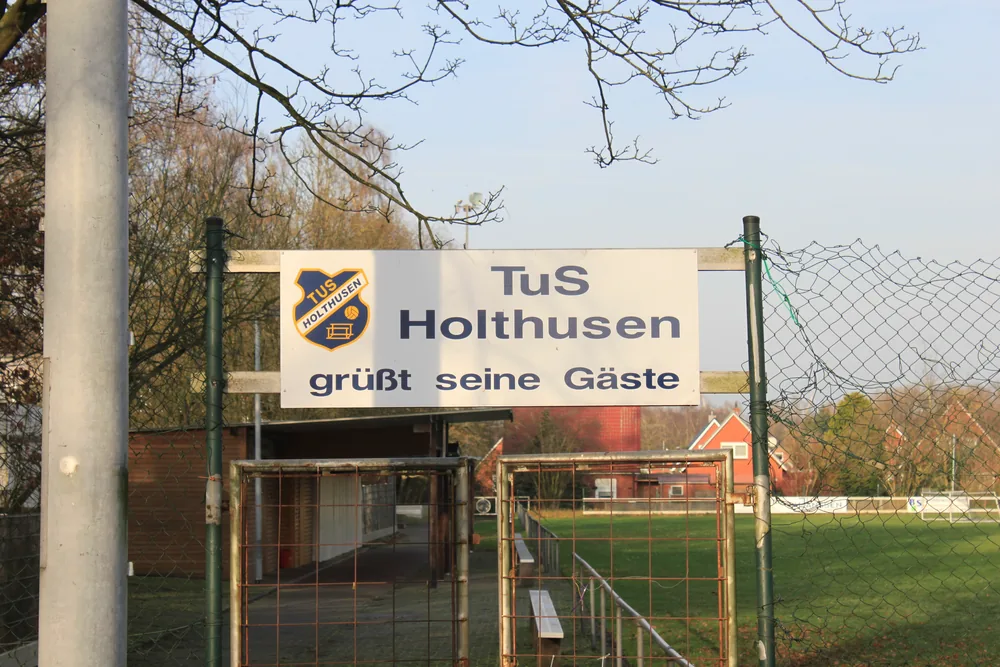 Eingang zum Sportplatz mit dem Schild „TuS Holthusen grüßt seine Gäste“