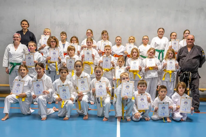 Die Selbstverteidigungsgruppe des TuS Holthusen in weißen Anzügen mit gelben, orangen und grünen Gürteln, die Kinder halten ihre Prüfungsurkunden in den Händen, links und rechts die Trainer